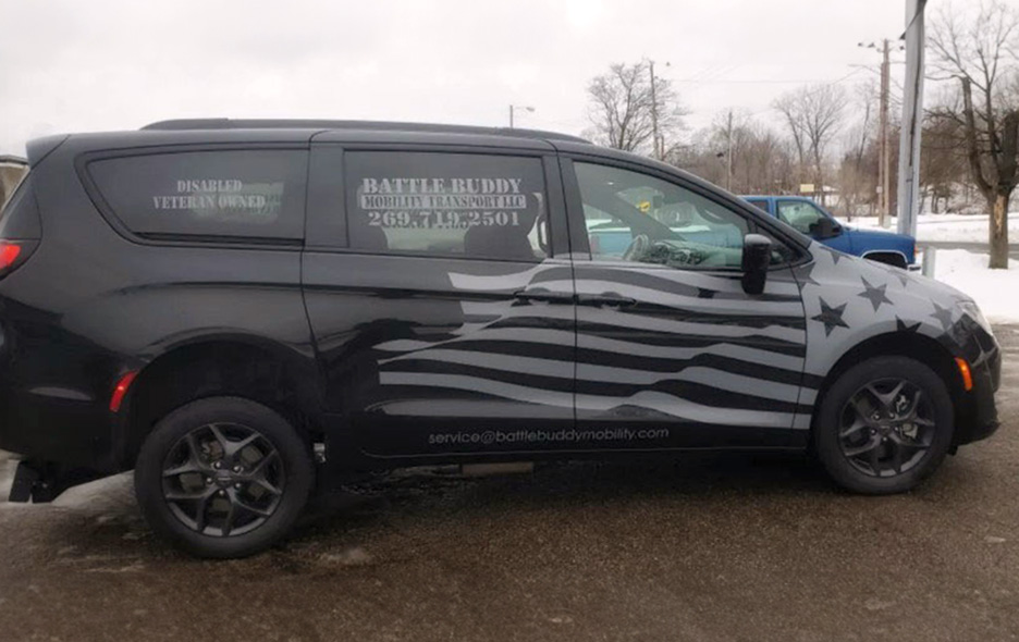 Image of the Battle Buddy van. A Black van with a gray American flag decal