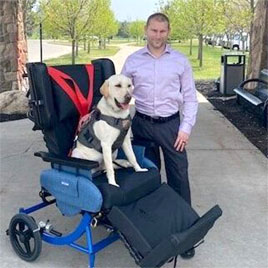 Photo of Kevin posing with his service dog and Broda chair