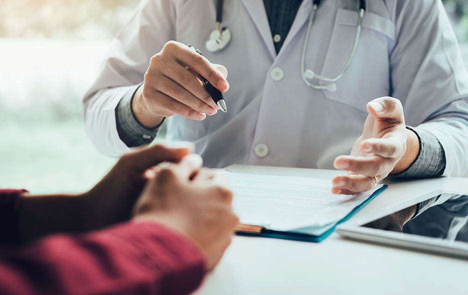 Close up of a doctor-patient chatting at a desk with paperwork