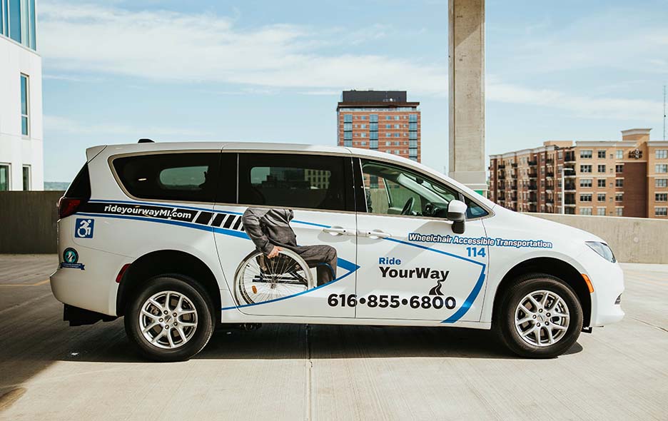 Side view of a Ride Your Way NEMT vehicle with a cityscape background